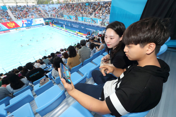 ▲광주세계수영선수권대회 참석한 관람객들이 KT 5G 네트워크를 이용해 핸드폰으로 경기 동영상을 감상하고 있다. ⓒKT