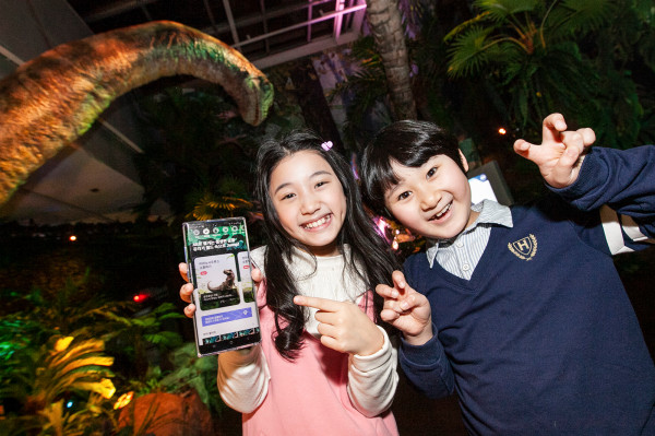 ▲SK텔레콤 홍보모델들이 롯데백화점 김포공항점에서 열린 ‘쥬라기 월드 특별전’에서 ‘Jump AR 동물원’ 공룡 캐릭터와 사진을 찍고 있다. ⓒSK텔레콤