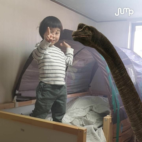 ▲어린이가 침대위에서 목을 빼고 있는 공룡(브라키오사우루스)과 나란히 서서 재밌는 표정을 짓고 있는 모습. ⓒSK텔레콤