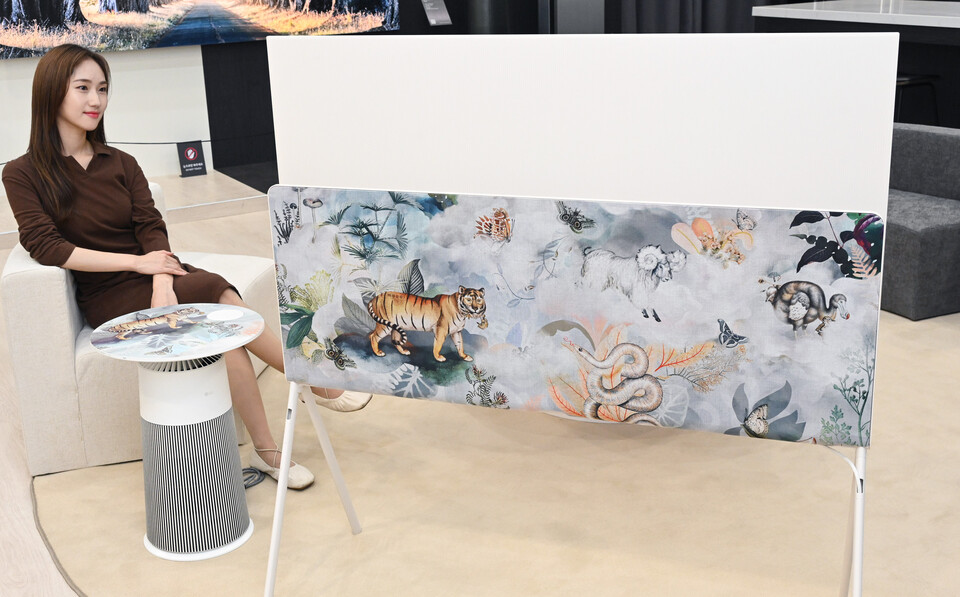 ▲LG전자 모델이 다양한 동물들이 아름답게 표현된 모오이의 대표 디자인을 적용한 라이프스타일 올레드 TV ‘포제’와 테이블형 공기청정기 ‘에어로퍼니처’를 체험하고 있다. ⓒLG전자